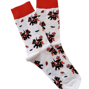 May include: A pair of white socks with a Halloween-themed print. The socks feature a black and orange pumpkin riding a black horse. The socks have red tops.