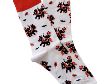 May include: A pair of white socks with a Halloween-themed print. The socks feature a black and orange pumpkin riding a black horse. The socks have red tops.