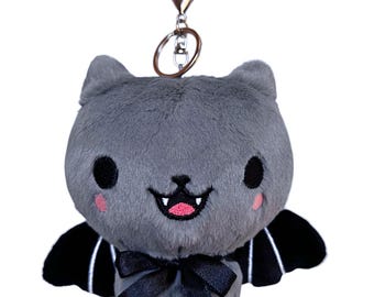 May include: A plush gray bat keychain with a black bow, black wings with white stripes, and a silver clasp. The bat has a smiling face with pink cheeks and a pink mouth. The keychain is designed to be a cute and spooky accessory.