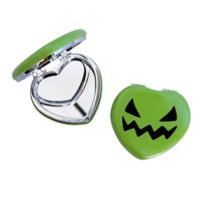 May include: Two heart-shaped compact mirrors. One is open, revealing a heart-shaped mirror. The other is closed, with a jack-o'-lantern face design. Both are lime green with silver trim.