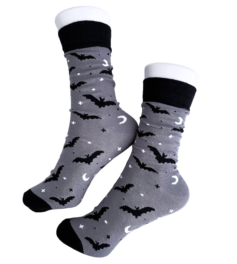 May include: A pair of gray socks with a black bat, moon, and star pattern. The socks have black cuffs, heels, and toes. The socks are displayed on white forms.