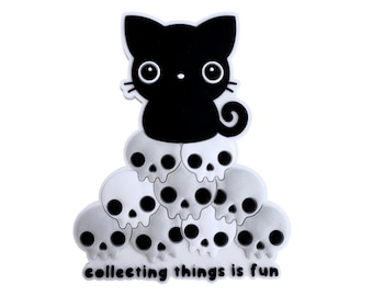 Puede incluir: Un pin de gato negro con grandes ojos blancos sentado sobre una pirámide de calaveras blancas. La base del pin presenta el texto negro "collecting things is fun" en una fuente redondeada. El diseño está realizado en un estilo plano.