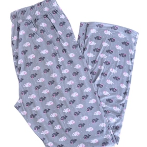 May include: Grey pajama trousers featuring a repeating pattern of white and dark grey sheep with pink details. The trousers have an elasticated waistband and a loose fit, ideal for sleep or relaxing at home.