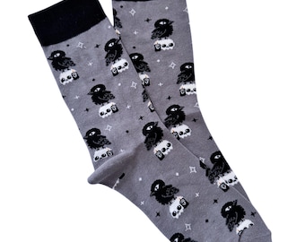 May include: A pair of gray socks with a black crow and skull pattern. The socks have a black cuff.