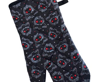 May include: Black oven mitt with a quilted design and a repeating pattern of cartoon black and red moth-like creatures with white stars on a black background.