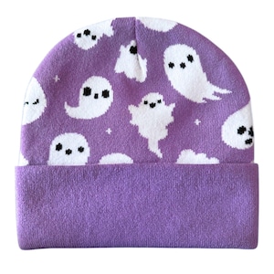 Puede incluir: Un gorro morado con un borde doblado. El gorro presenta un patr&oacute;n repetido de fantasmas de dibujos animados blancos con ojos y bocas negras. Los fantasmas est&aacute;n dispersos por la superficie del gorro, creando un dise&ntilde;o l&uacute;dico. El borde es de un tono morado m&aacute;s oscuro.