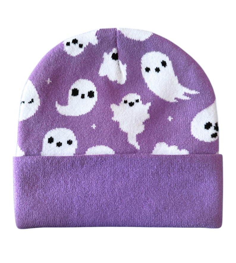 Puede incluir: Un gorro morado con un borde doblado. El gorro presenta un patr&oacute;n repetido de fantasmas de dibujos animados blancos con ojos y bocas negras. Los fantasmas est&aacute;n dispersos por la superficie del gorro, creando un dise&ntilde;o l&uacute;dico. El borde es de un tono morado m&aacute;s oscuro.