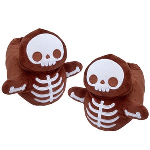 May include: A pair of brown plush skeleton slippers with white embroidered details. The slippers feature a skull design on the top and a skeleton design on the bottom.