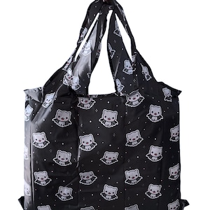 May include: Black reusable shopping bag with a repeating pattern of cartoon bat-cats. The bat-cats are gray with white accents and small red hearts. The bag has black handles and is made of a lightweight, foldable material.