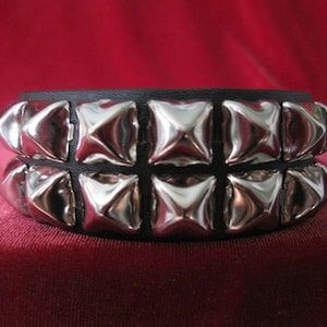 Puede incluir: Un brazalete de cuero negro con dos filas de tachuelas piramidales plateadas.