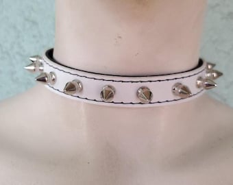 May include: White leather choker with silver spikes. The choker is about 1 inch wide and has a stitched edge.