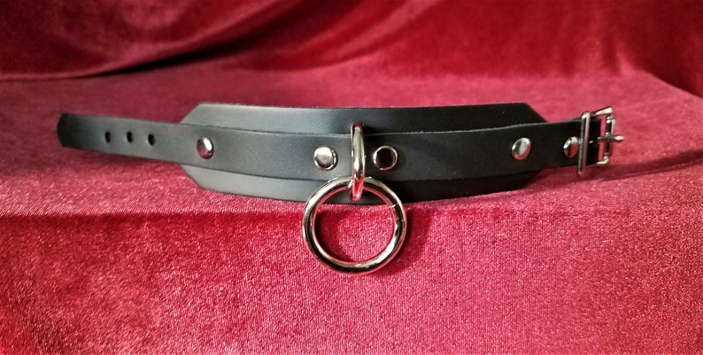 May include: Black leather choker with silver hardware, including a large ring and a buckle closure.