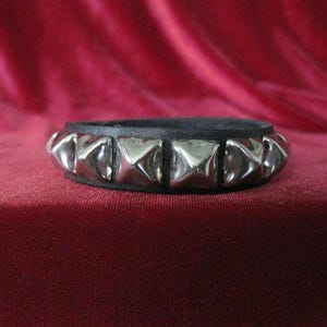 Könnte beinhalten: Ein schwarzes Lederarmband mit silbernen pyramidenförmigen Nieten.