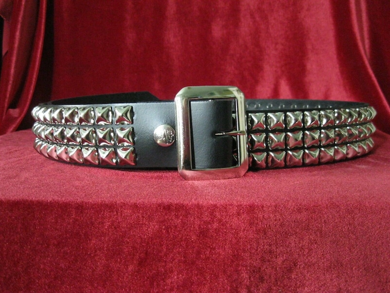 May include: A black leather belt with three rows of silver pyramid-shaped studs. The belt has a silver buckle.