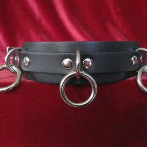May include: Black leather choker with three silver rings and silver studs.