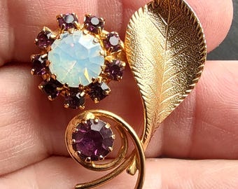 Precioso broche floral con piedras moradas, imitación de ópalo y bisutería dorada.