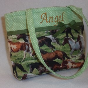 Pode incluir: Pequena sacola com tecido tem&aacute;tico de cavalos. A sacola apresenta acabamento e al&ccedil;as de bolinhas verdes, com o nome "Angel" bordado em fio dourado. Um la&ccedil;o verde adiciona um toque decorativo.