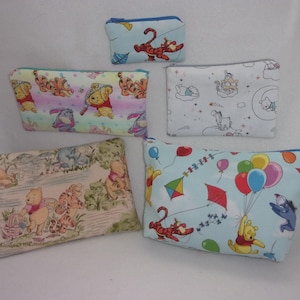May include: Five zippered pouches with various Winnie the Pooh character designs. The pouches feature illustrations of Pooh, Tigger, Eeyore, and Piglet. The pouches are in various sizes and have different background colors.