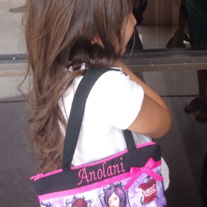 May include: A purple and pink tote bag with a black strap and the name "Anolani" embroidered on the front. The bag features a print of characters from the Disney movie "Descendants".