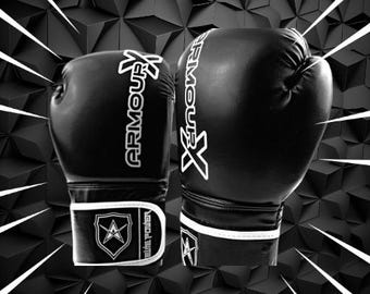 Puede incluir: Un par de guantes de boxeo negros con ribetes blancos y el texto "ARMOUR X" en el lateral. Los guantes tienen un logotipo de escudo blanco con una estrella en la correa de la muñeca.