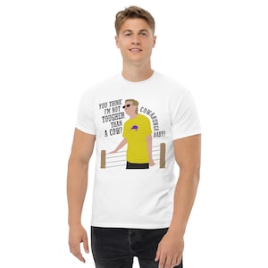May include: White t-shirt with a cartoon illustration of a man wearing a yellow shirt and sunglasses. The text on the shirt reads "You think I'm not tougher than a cow?  Cowabunga Baby!"