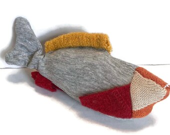 May include: A gray, red, orange, and yellow handmade stuffed fish toy. The fish is made from fabric scraps and has a simple design.