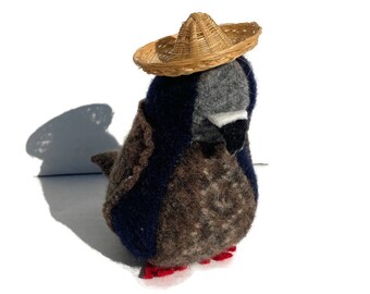 May include: A brown and gray plush bird wearing a small straw sombrero. The bird has red felt feet.