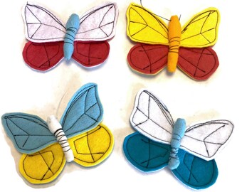 May include: Four felt butterflies in different color combinations. The butterflies are red, yellow, blue, and white. They are all sewn with black thread.