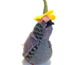 May include: A small, gray and purple bird with a black beak, wearing a yellow flower hat with a green stem.