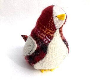 May include: A small, handmade bird toy made from red and white fabric with a yellow beak. The bird has a plaid pattern on its back and a white belly.