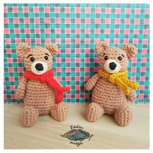 Puede incluir: Dos osos de peluche tejidos a crochet, uno con una bufanda roja y el otro con una bufanda amarilla, sentados sobre un fondo a cuadros. Los osos tienen pelaje marrón y ojos negros. El texto "L'atelier nuage" es visible en la parte inferior central de la imagen.