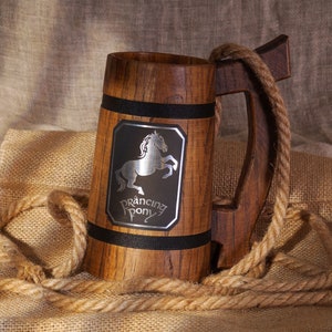 Könnte beinhalten: Ein Bierkrug aus Holz mit einem schwarzen Band und einem silbernen Metallemblem mit einem galoppierenden Pferd und dem Text "Prancing Pony".