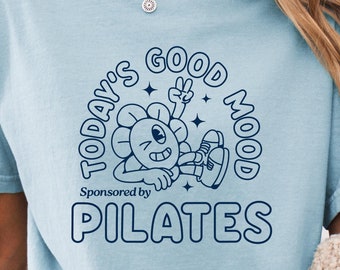 May include: A light blue t-shirt with a graphic of a cartoon flower with the text "Today's Good Mood Sponsored by PILATES".