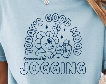 May include: A light blue t-shirt featuring a cartoon flower with a peace sign and the text "Today's Good Mood Sponsored by Jogging".