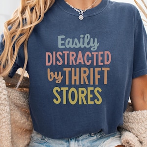 May include: A navy blue t-shirt with the text "Easily Distracted by Thrift Stores" in a rainbow color scheme.