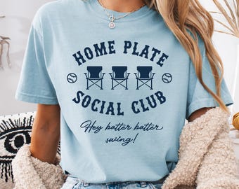 May include: Light blue t-shirt with a navy blue graphic that says "Home Plate Social Club" with three chairs and baseballs. The text "Hey batter batter swing!" is below the graphic.