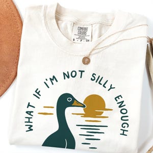 Puede incluir: Una camiseta blanca con una ilustración de ganso verde y el texto "What if I'm not silly enough".