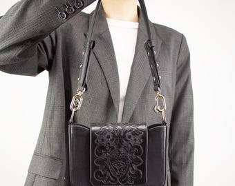 May include: A black leather shoulder bag with a gold chain strap and an embossed floral design. The bag has a flap closure and a small pocket on the front.
