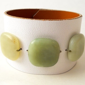 White leather bracelet with three green jade stone beads. The inside of this leather bracelet is lined with soft caramel colored leather which peeks out ever so subtly when you wear it. A single  metal snap is used to fasten the bracelet into place.