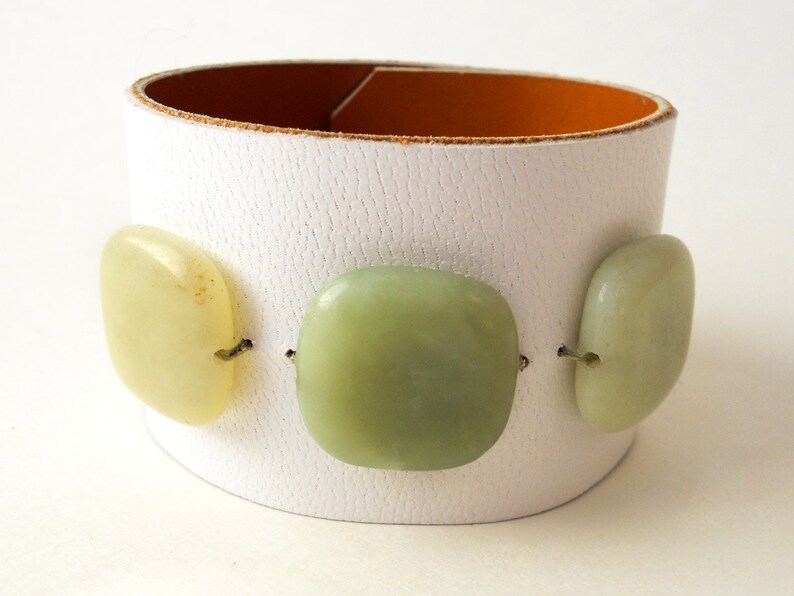 White leather bracelet with three green jade stone beads. The inside of this leather bracelet is lined with soft caramel colored leather which peeks out ever so subtly when you wear it. A single  metal snap is used to fasten the bracelet into place.