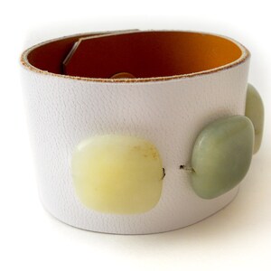 White leather bracelet with three green jade stone beads. The inside of this leather bracelet is lined with soft caramel colored leather which peeks out ever so subtly when you wear it. A single  metal snap is used to fasten the bracelet into place.