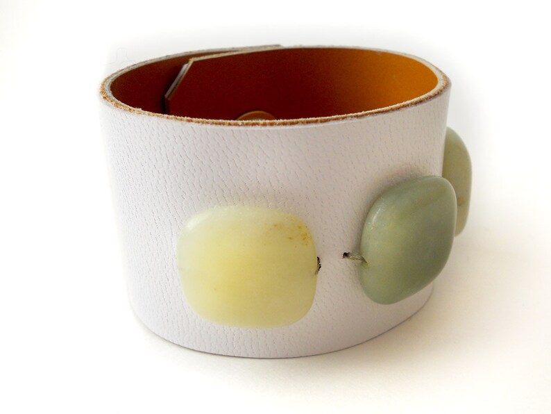 White leather bracelet with three green jade stone beads. The inside of this leather bracelet is lined with soft caramel colored leather which peeks out ever so subtly when you wear it. A single  metal snap is used to fasten the bracelet into place.