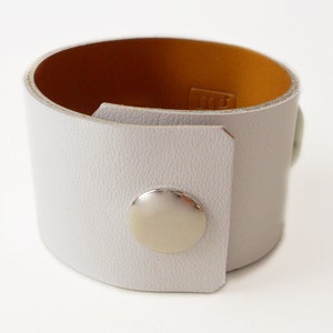 White leather bracelet with three green jade stone beads. The inside of this leather bracelet is lined with soft caramel colored leather which peeks out ever so subtly when you wear it. A single  metal snap is used to fasten the bracelet into place.
