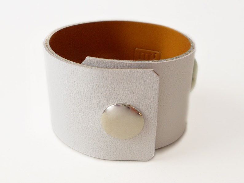 White leather bracelet with three green jade stone beads. The inside of this leather bracelet is lined with soft caramel colored leather which peeks out ever so subtly when you wear it. A single  metal snap is used to fasten the bracelet into place.