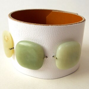 White leather bracelet with three green jade stone beads. The inside of this leather bracelet is lined with soft caramel colored leather which peeks out ever so subtly when you wear it. A single  metal snap is used to fasten the bracelet into place.