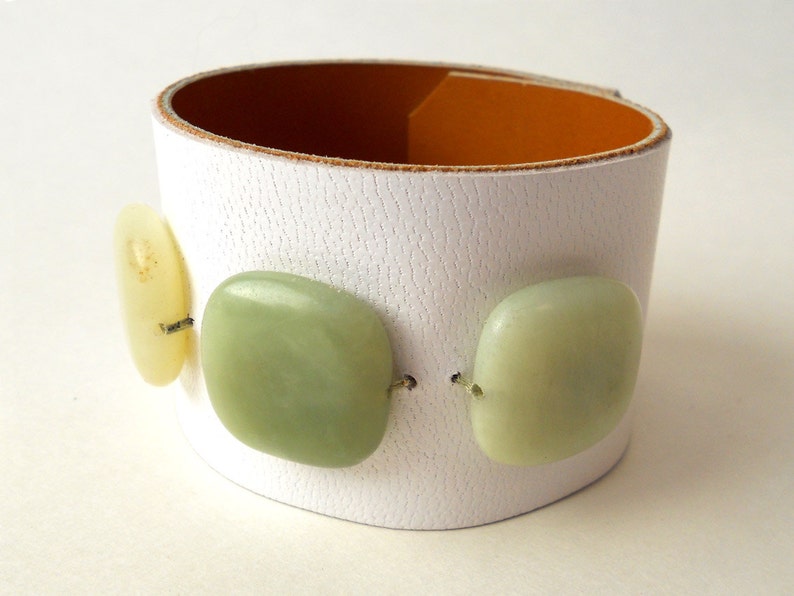 White leather bracelet with three green jade stone beads. The inside of this leather bracelet is lined with soft caramel colored leather which peeks out ever so subtly when you wear it. A single  metal snap is used to fasten the bracelet into place.