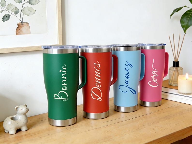 Puede incluir: Cuatro vasos personalizados en verde, rojo, azul claro y rosa, cada uno con borde y asa plateados. Los nombres "Bonnie", "Dennis", "James" y "Cora" est&aacute;n escritos en cursiva en cada vaso.