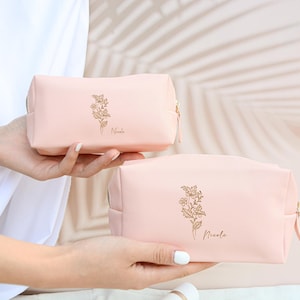 May include: Two pink zippered cosmetic bags with gold floral designs and the name "Nicole" printed on each.