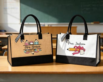 Peut inclure: Deux sacs fourre-tout rectangulaires avec des anses et une base noirs. Le sac de gauche est en toile de jute beige avec un motif de crayons et le texte "Mrs. Brown". Le sac de droite est en toile blanche avec un motif de crayon orné d'un nœud rose et le texte "Mrs. Jackson". Chaque sac possède un ruban rayé noir et blanc attaché à une anse.