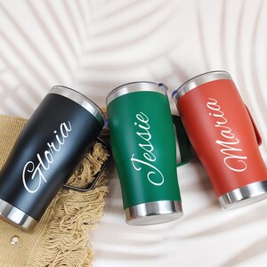 Puede incluir: Tres vasos personalizados de acero inoxidable en negro, verde y rojo. Cada vaso tiene un asa y un borde plateado. Los nombres "Gloria", "Jessie" y "Maria" est&aacute;n escritos en blanco en cada vaso.